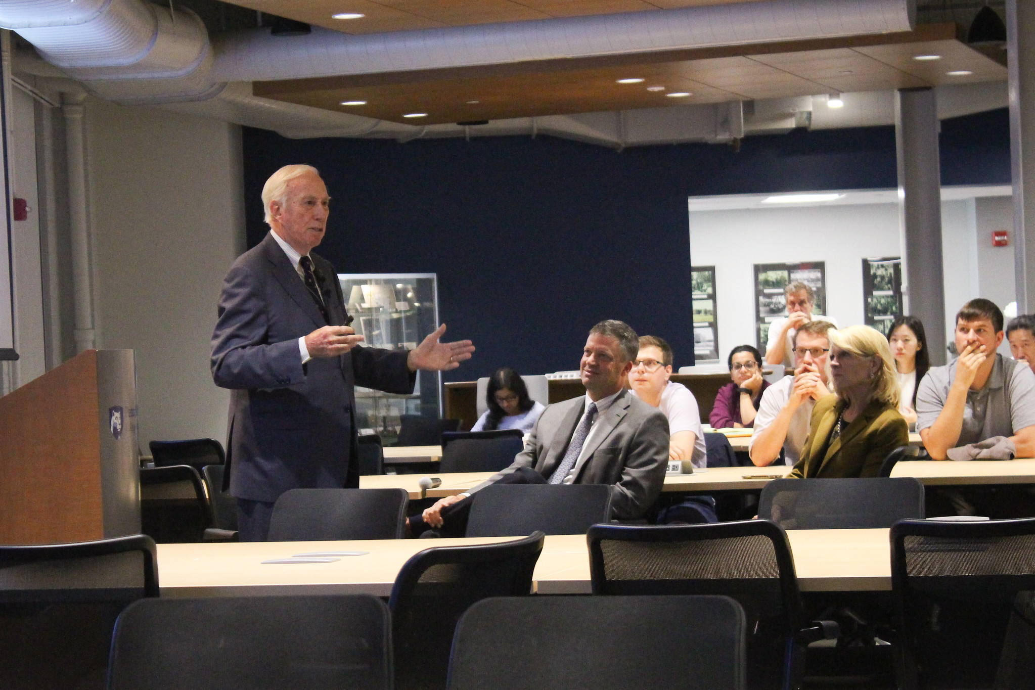 A Caucasian man addresses a group of people during a lecture.